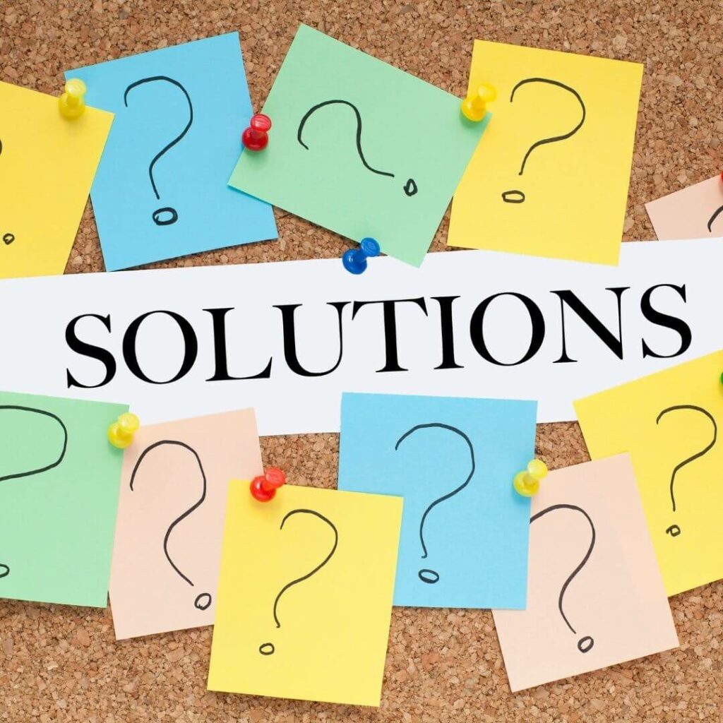 Das Bild zeigt eine Korkwand, auf denen sich viele bunte Zettel mit Fragezeichen befinden. Über den bunten Zetteln steht das Wort Solutions. Übersetzt heißt das Wort Lösungen.